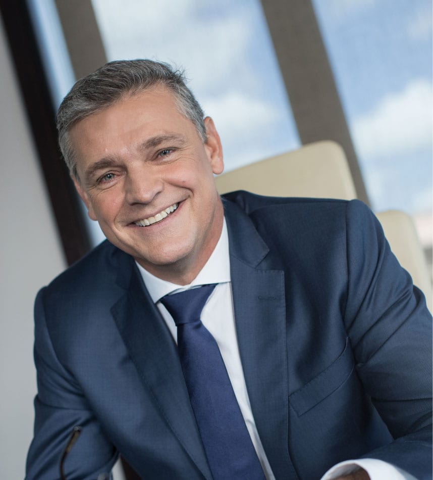 Formal portrait of Arnaud Lagesse in a navy suit, smiling, seated indoors in Mauritius