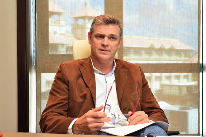 Arnaud Lagesse working at his desk in a tan jacket, holding his reading glasses