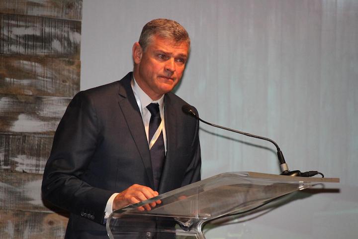 Arnaud Lagesse speaking from a clear podium with a microphone at an evening event