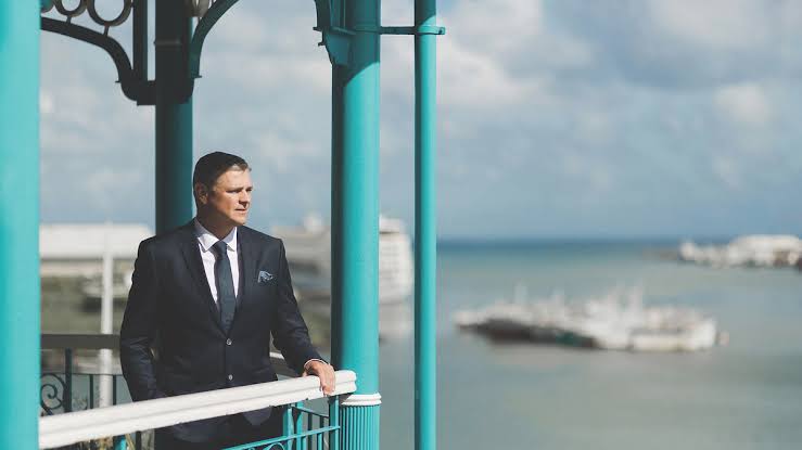 Arnaud Lagesse standing on a colonial-style balcony overlooking the harbour in Mauritius